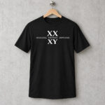 XX XY Shirt, Original Factory Settings white print on a black T-shirt hanging on a wooden hanger against a concrete wall